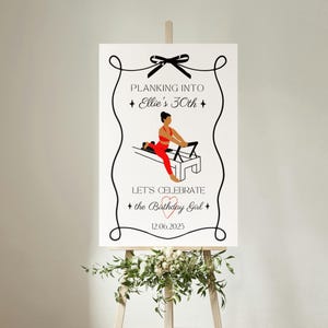 Może przedstawiać: Biały znak na sztaludze z napisem "Planking into Ellie's 30th" i "Let's Celebrate the Birthday Girl". Znak zawiera czarną kokardę, ozdobne wiry i ilustrację osoby na maszynie do pilatesu. Data 12.06.2025 jest r&oacute;wnież uwzględniona.