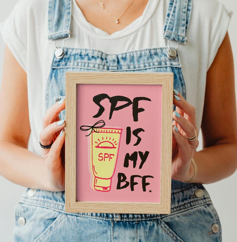 May include: A framed print with a pink background and the text "SPF is my BFF."  A cartoon illustration of a yellow sunscreen bottle with a red sun and the word "SPF" is shown.