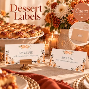 May include: Two white rectangular folded dessert labels featuring orange and white floral illustrations. The text reads APPLE PIE with cinnamon & a flaky crust. One label is held by a gold metal stand, while the other stands independently.