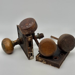 May include: Antique door hardware set featuring two doorknobs and a latch mechanism. The doorknobs are made of wood and have a round shape. The metal latch plate is rectangular and shows signs of age and wear.