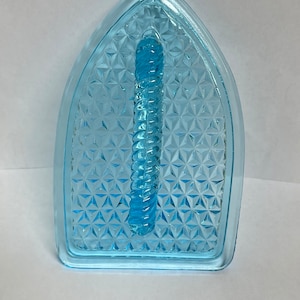 May include: A light blue glass iron rest with a diamond pattern. The iron rest has a raised handle in the center.
