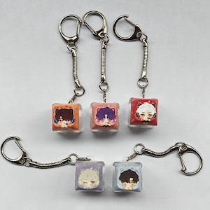 Peut inclure: Plusieurs porte-clés avec des breloques cubiques transparentes. Chaque breloque présente un personnage de style anime coloré. Les porte-clés ont des fermoirs en métal argenté et des attaches à ressort hélicoïdal. Les personnages ont des cheveux et des tenues différents.