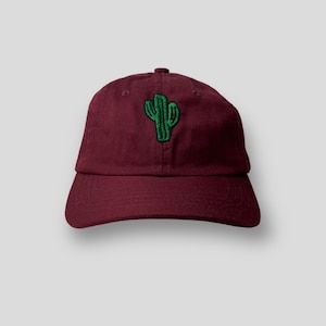 Op de afbeelding: Een marineblauwe baseballpet met een groen geborduurd cactusontwerp.