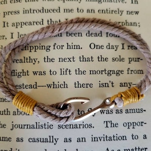 May include: A nautical-themed bracelet featuring a gray rope design with yellow accents and a silver hook clasp. The bracelet is displayed on a book page, showcasing a classic and rugged style. This accessory is suitable for everyday wear.