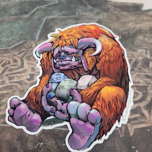 May include: A sticker illustration of a furry orange monster with purple skin and horns, sitting down and holding three gray stones. The stones are inscribed with the letters FR, IE, and NDS, collectively spelling the word FRIENDS.