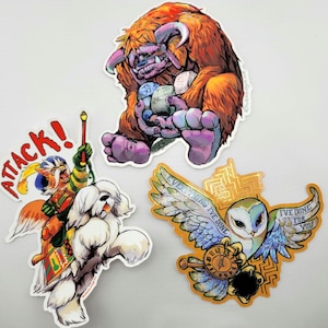 May include: Three die-cut stickers featuring fantasy illustrations. One shows a furry orange monster holding spheres, another depicts a cat-like warrior riding a white dog with the text ATTACK!, and the third shows an owl with the text EVERYTHING I'VE DONE I'VE DONE FOR YOU.