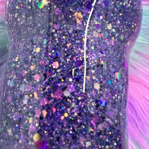 Pu&ograve; includere: Primo piano di un bicchiere con glitter viola. Il bicchiere &egrave; ricoperto da una moltitudine di pezzi di glitter di varie dimensioni e colori, tra cui viola, oro e iridescente. I glitter sono fittamente impacchettati, creando un effetto scintillante.