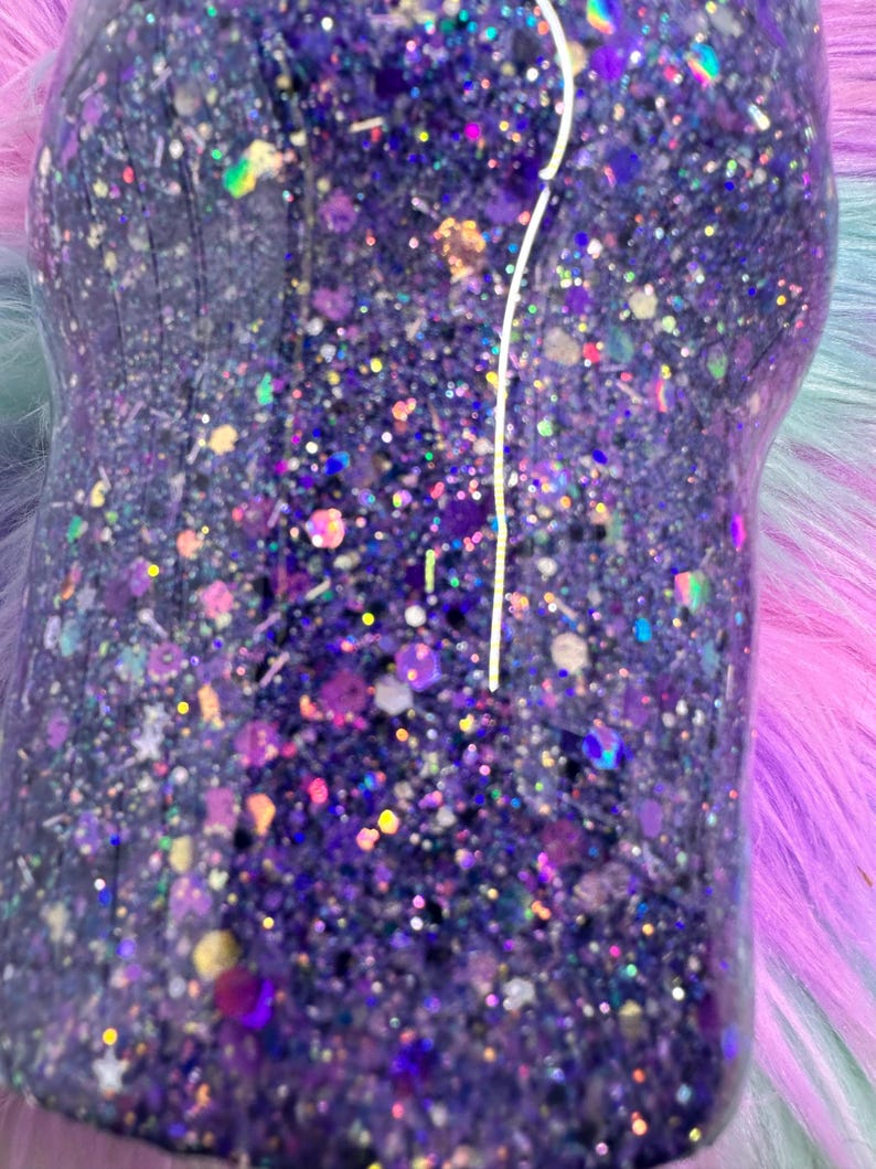 Pu&ograve; includere: Primo piano di un bicchiere con glitter viola. Il bicchiere &egrave; ricoperto da una moltitudine di pezzi di glitter di varie dimensioni e colori, tra cui viola, oro e iridescente. I glitter sono fittamente impacchettati, creando un effetto scintillante.