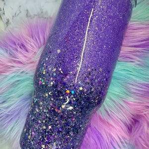 Pu&ograve; includere: Un bicchiere viola glitterato con un effetto sfumato, che passa da una tonalit&agrave; pi&ugrave; chiara nella parte superiore a una tonalit&agrave; pi&ugrave; scura nella parte inferiore. Il bicchiere &egrave; cilindrico e ha un coperchio nero.