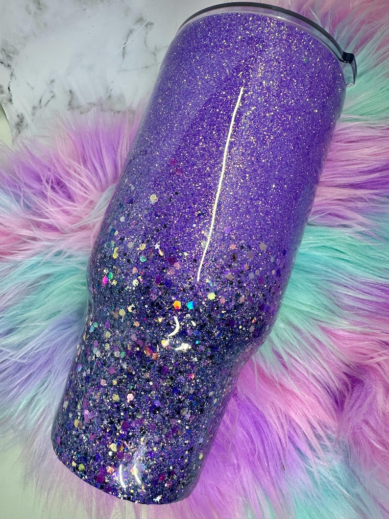 Pu&ograve; includere: Un bicchiere viola glitterato con un effetto sfumato, che passa da una tonalit&agrave; pi&ugrave; chiara nella parte superiore a una tonalit&agrave; pi&ugrave; scura nella parte inferiore. Il bicchiere &egrave; cilindrico e ha un coperchio nero.