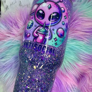 Pu&ograve; includere: Un bicchiere glitterato viola con un disegno alieno e la scritta "ANTISOCIAL". L'alieno sta bevendo da una tazza. Il bicchiere &egrave; ricoperto di glitter viola, con un effetto sfumato.