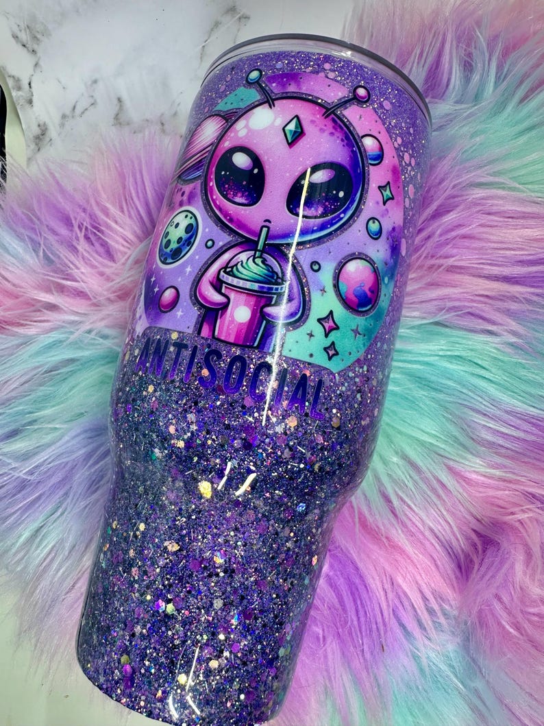 Pu&ograve; includere: Un bicchiere glitterato viola con un disegno alieno e la scritta "ANTISOCIAL". L'alieno sta bevendo da una tazza. Il bicchiere &egrave; ricoperto di glitter viola, con un effetto sfumato.