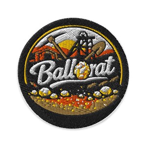 May include: A circular embroidered patch featuring a black border and a central design of a mining structure, a pickaxe, and a shovel. The text Ballarat is stitched in white across the middle, with orange and yellow ground details below.
