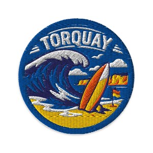 May include: A circular embroidered patch featuring a blue ocean wave, a yellow and orange surfboard, and a sandy beach. The word TORQUAY is stitched in white capital letters across the top of the design, with small white clouds in the sky.