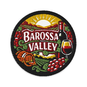 May include: A circular embroidered patch featuring a landscape of the Barossa Valley with a sun, grapevines, a wine bottle, and a glass of red wine. The text 'BAROSSA VALLEY' is embroidered in white across a red banner in the centre of the design.