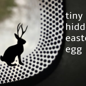 May include: A black silhouette of a rabbit with antlers is hidden within a white and black polka dot pattern. The text "tiny hidden easter egg" is written in white on a black background.