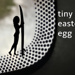 May include: A black silhouette of a person holding a surfboard with the text "tiny easter egg" on a black background.