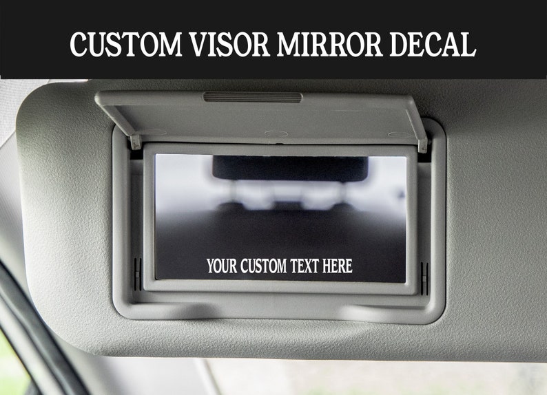K&ouml;nnte beinhalten: Ein grauer Auto-Sonnenblendenspiegel mit einem schwarzen rechteckigen Aufkleber, auf dem "YOUR CUSTOM TEXT HERE" steht.