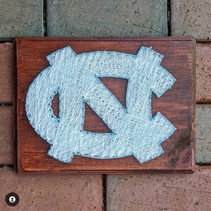 May include: A wooden plaque with a blue and white string art design of the letters "NC".