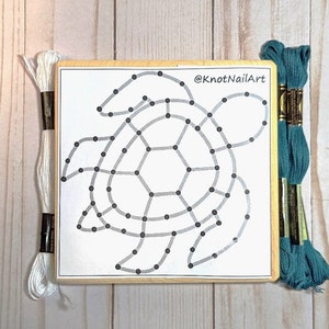 May include: A wooden craft kit with a printed outline of a turtle. The kit includes white and teal embroidery floss. The text '@KnotNailArt' is printed on the wood.