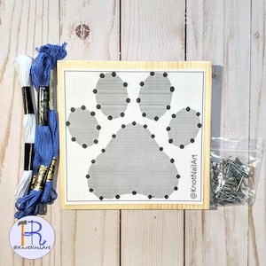 May include: A wooden craft kit with a paw print design, two spools of embroidery floss, one white and one blue, and a bag of nails. The kit includes instructions for string art. The text on the wood reads "@KnotNailArt".