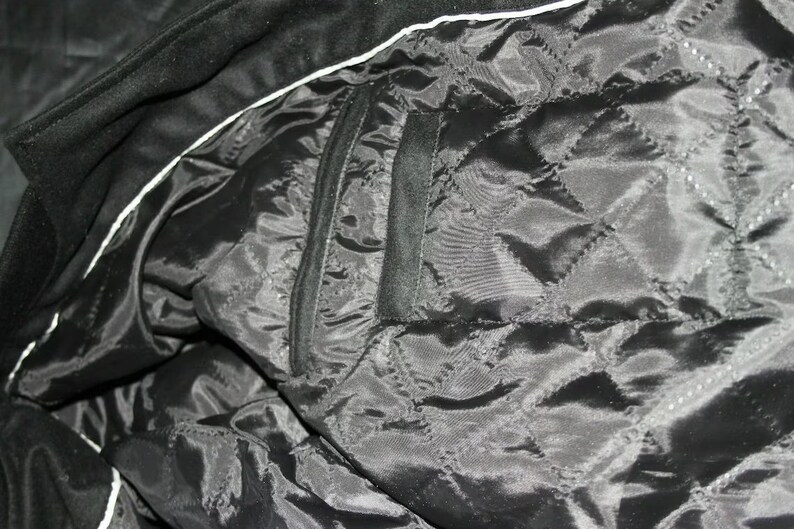 May include: Black quilted lining of a jacket with a black pocket. The lining has a diamond pattern.