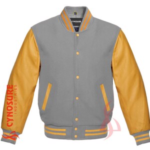 May include: A gray and gold varsity jacket with a ribbed collar and cuffs. The sleeves are made of brown leather and have the text "CYNOSURE INDUSTRIES" printed on the left sleeve. The jacket has a button closure and two pockets.