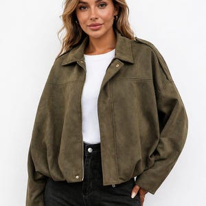 Può includere: Giacca in camoscio verde oliva con collo, chiusura con zip e dettagli con bottoni. La giacca ha una vestibilità ampia ed è abbinata a jeans neri e un top bianco.