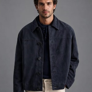 Pu&ograve; includere: Una giacca in camoscio blu navy con chiusura a bottoni e colletto. La giacca &egrave; abbinata a una camicia blu scuro e pantaloni beige chiaro. Il design della giacca &egrave; semplice e classico, adatta a varie occasioni.