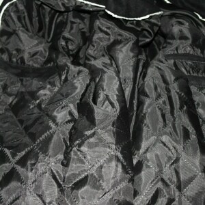 May include: Black quilted lining of a jacket with a white trim around the edges.