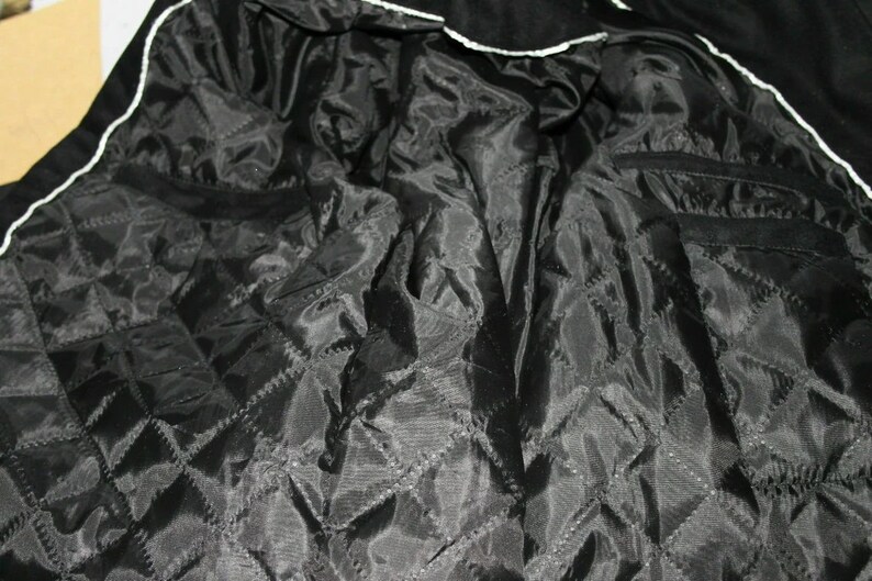 May include: Black quilted lining of a jacket with a white trim around the edges.