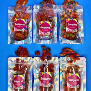 May include: Six clear plastic bags with colorful candy inside. Each bag has a label with the text "Goosgueras" and a logo. The candy is a variety of shapes and colors, including red, green, and yellow.
