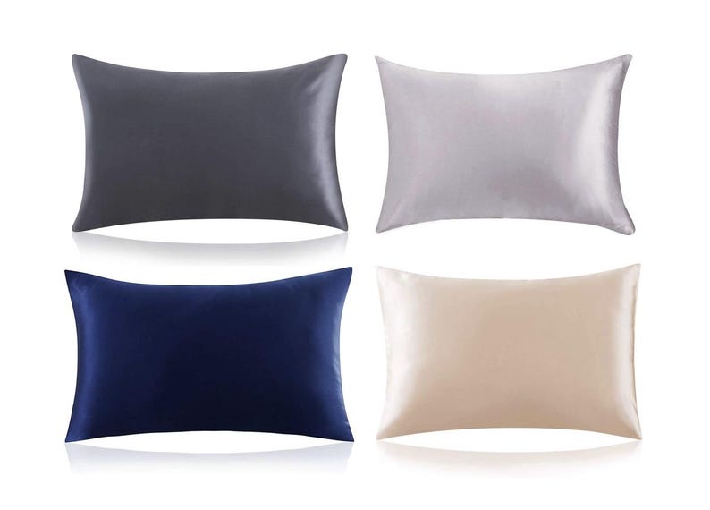 K&ouml;nnte beinhalten: Vier Satin-Kissenbez&uuml;ge in verschiedenen Farben: Grau, Silber, Marineblau und Beige. Die Kissenbez&uuml;ge sind in zwei Reihen zu je zwei angeordnet.