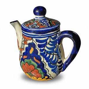 May include: A ceramic teapot with a lid, featuring a vibrant hand-painted design. The teapot showcases a white base adorned with blue, orange, and green floral patterns. The handle and lid are a deep blue, creating a striking contrast.