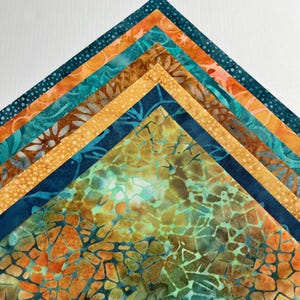 May include: A stack of six triangular fabric swatches arranged in a layered chevron pattern. The fabrics feature batik-style prints in shades of teal, orange, brown, and yellow, with patterns including dots, floral motifs, and a cracked stone design.