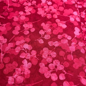 May include: Red fabric with a pink floral pattern. The fabric has a batik style design with a dark red background and pink leaves and flowers.