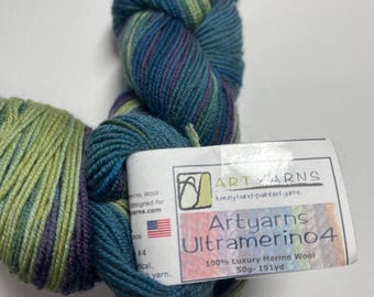 May include: A skein of hand-painted yarn in shades of teal, purple, and green. The label reads "Artyarns Ultramerino4" and "100% Luxury Merino Wool, 50g - 191yd". The yarn is designed for knitting and other fiber arts.