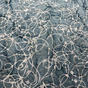 May include: Close-up of a fabric with a blue-gray background and a white, abstract, swirling pattern. The design resembles interconnected lines and organic shapes, creating a textured appearance. The fabric has a slightly mottled effect.