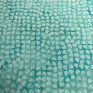 May include: Close-up of a teal fabric with a pattern of small, white, irregular shapes. The shapes are densely packed across the surface, creating a textured appearance. The fabric has a mottled effect, with variations in the teal color.