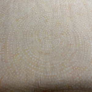 May include: A close-up of a fabric with a repeating pattern of small white dots on a light peach background. The fabric is folded, showing texture and depth. The overall design is soft and organic.