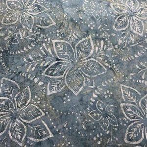May include: A blue fabric featuring a white batik-style floral pattern with five-petaled flowers and small dots. The material has a mottled, textured appearance with varying shades of blue and grey, creating a layered, hand-dyed visual effect.
