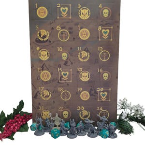 May include: A brown rectangular advent calendar featuring a grid of twenty-four numbered squares with gold icons including skulls, hearts, helmets, and axes. A collection of small grey fantasy character figurines and teal dice are arranged in front.