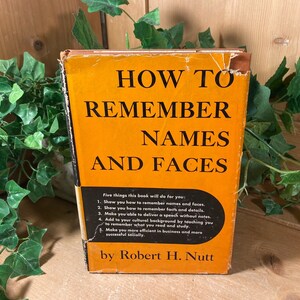May include: An orange book titled "How to Remember Names and Faces" by Robert H. Nutt. The book cover lists five things the book will do for you: show you how to remember names and faces, remember facts and details, deliver a speech without notes, add to your cultural background, and make you more efficient in business and successful socially.