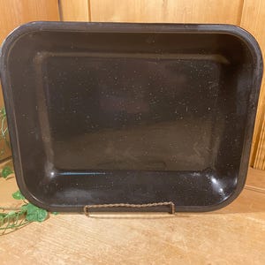 May include: A rectangular black roasting pan with a speckled white finish. The pan features rounded corners, a deep basin, and a smooth, glossy surface. It is constructed with a wide, flat rim and is presented in a simple, functional design.