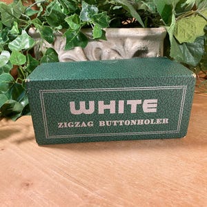 May include: A green box with the text "WHITE ZIGZAG BUTTONHOLER" in white lettering.