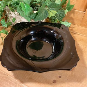 May include: A black glass serving bowl with a scalloped rim. The bowl is empty and has a reflective surface.