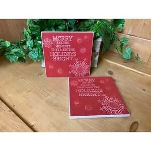 May include: Two red ceramic coasters with white snowflake designs and the text "Merry are the moments that make the holidays bright."