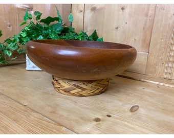 May include: A large, dark brown wooden bowl with a woven base. The bowl is round and has a smooth, polished finish.