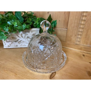 May include: A clear glass dome with a decorative pattern, used for covering and protecting food. The dome has a knob on top and sits on a matching base.