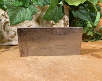 May include: A silver metal rectangular box with the text "Manufactured for the U.S. Navy by the Anchor Cap & Closure Corp. of Long Island City, N.Y."